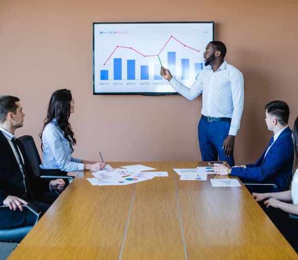 A strategic meeting in progress, with a presenter pointing to a screen with charts in a modern conference room.
